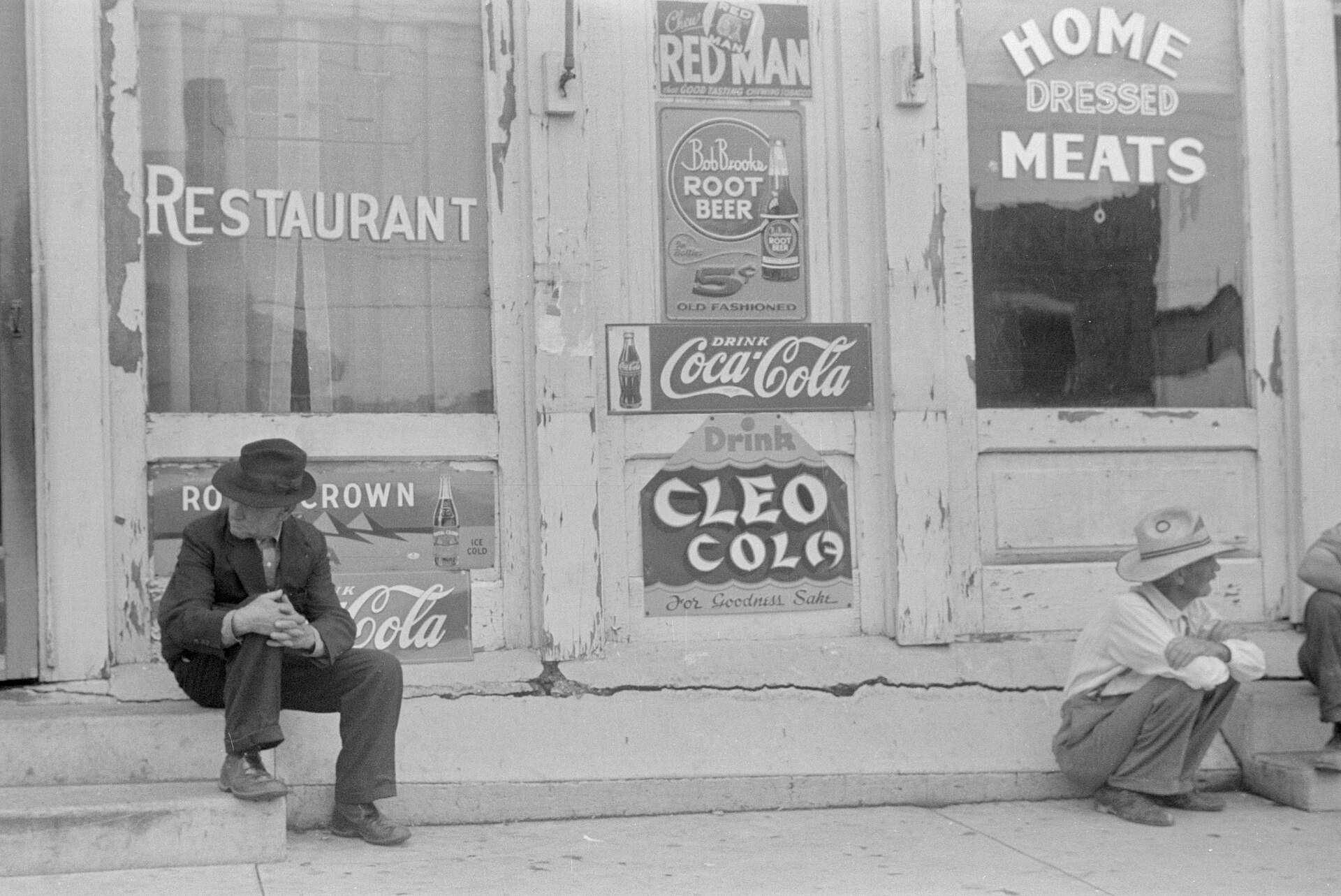 Ben Shahn, Worthington, Ohio, août 1938 : devanture peinte, réclames Coca-Cola et Cleo Cola, deux hommes assis sur le trottoir