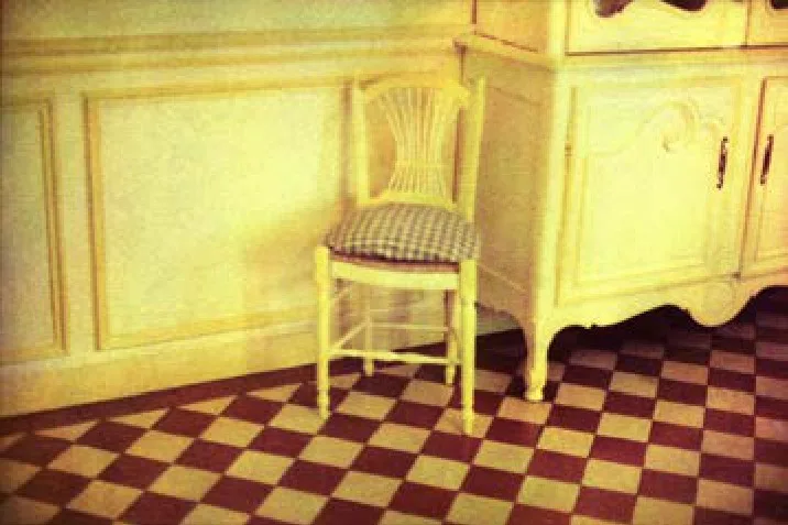 La salle à manger jaune de Monet, une chaise cannée, le sol en damier rouge et ocre