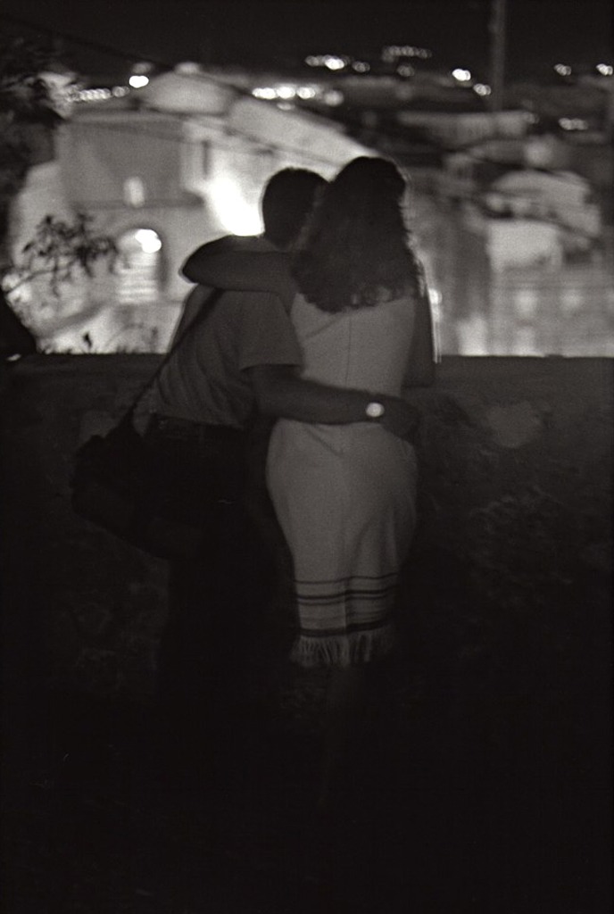 De nuit, un couple enlacé de dos, les lumières de la ville derrière, image tremblée