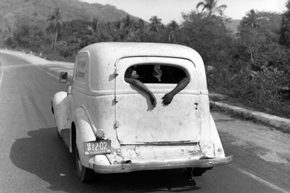 Voiture vue de l'arrière sur une route, deux bras pendant par la vitre arrière