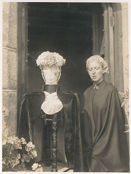 Claude Cahun en cape auprès d'une figure encapuchonnée et de deux bustes