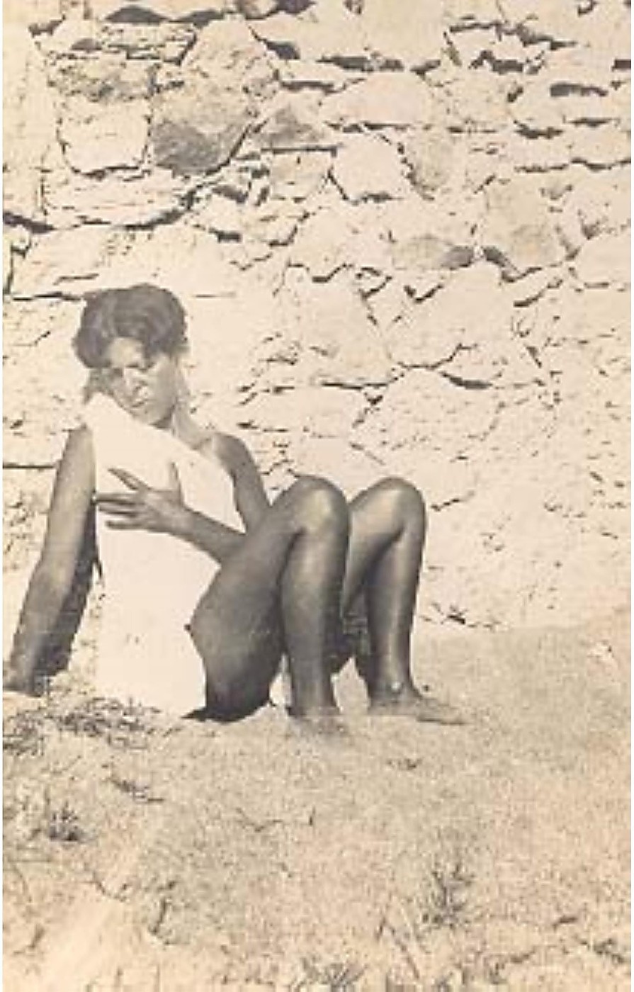 Claude Cahun assise en collants sombres, la main posée sur la poitrine