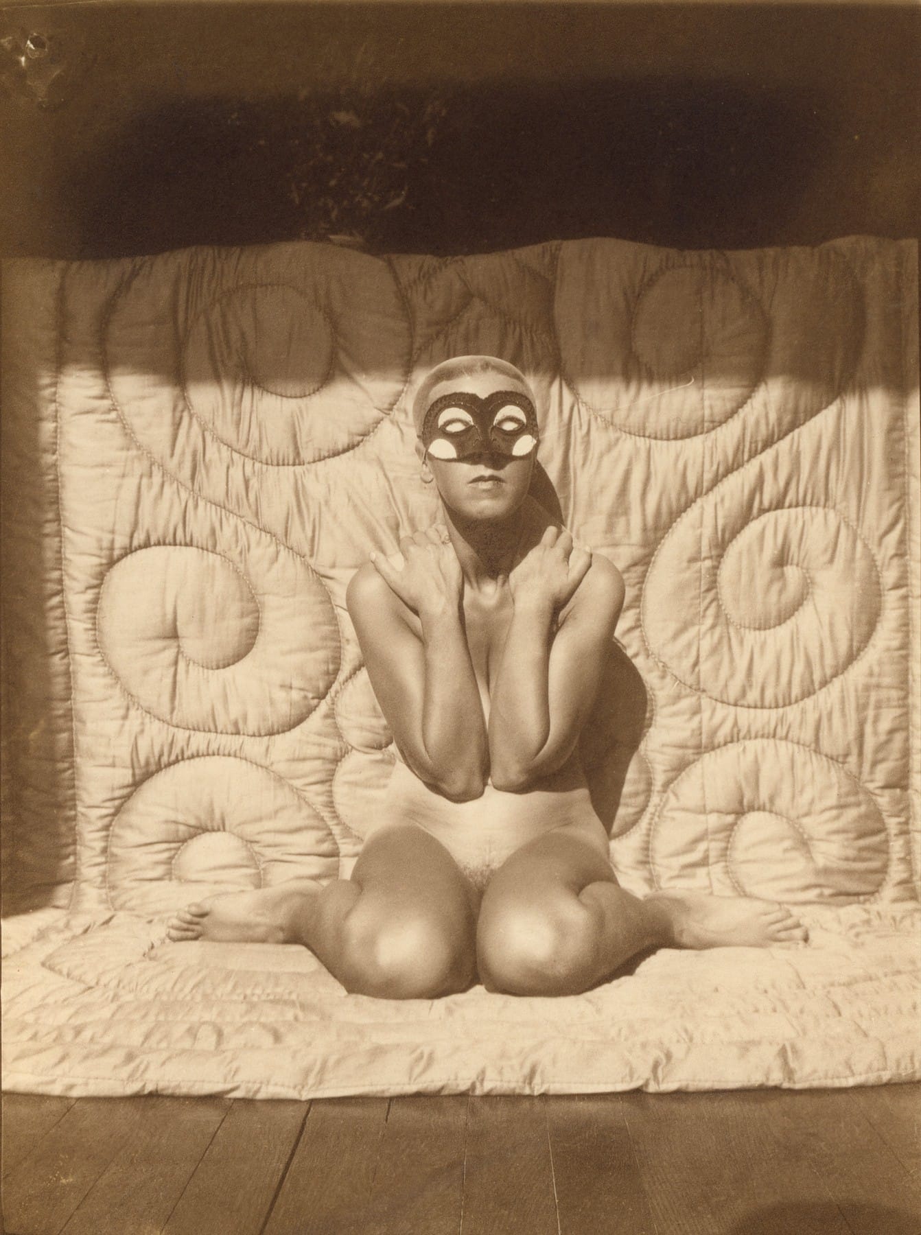 Claude Cahun agenouillée, nue et masquée, devant un bas-relief sculpté