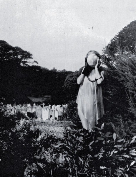 Claude Cahun tenant un masque à la main, dans un jardin