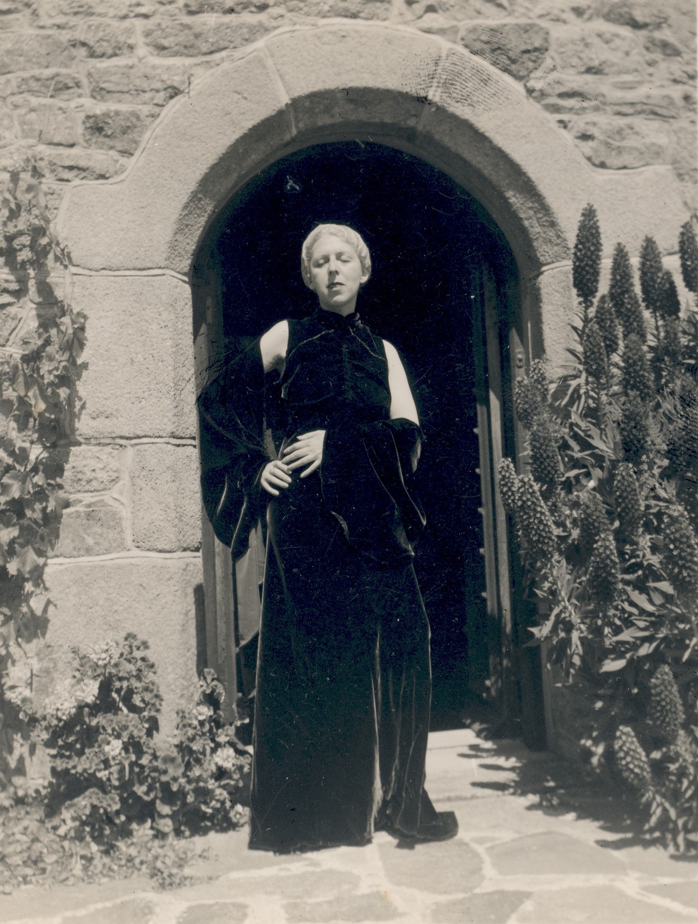 Claude Cahun en robe de velours devant l'arche de La Rocquaise