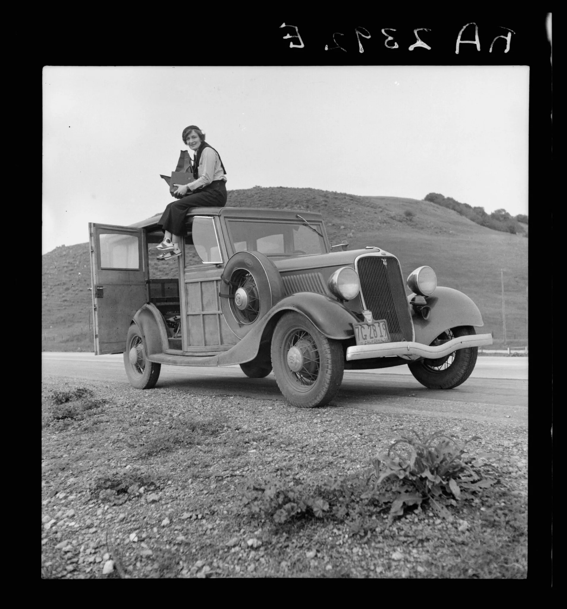 Dorothea Lange perchée sur sa voiture, appareil en main, Californie