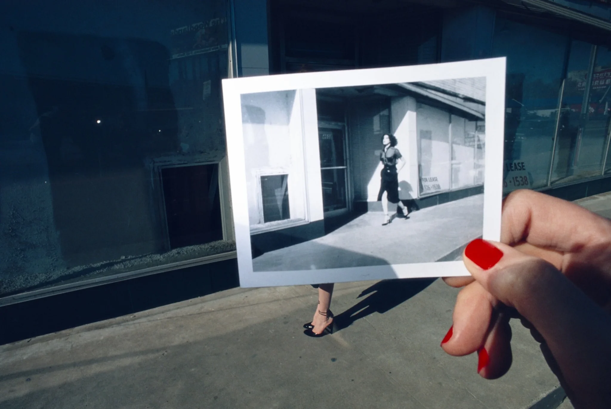 Main aux ongles rouges tenant une photographie devant une vitrine, campagne Charles Jourdan par Guy Bourdin