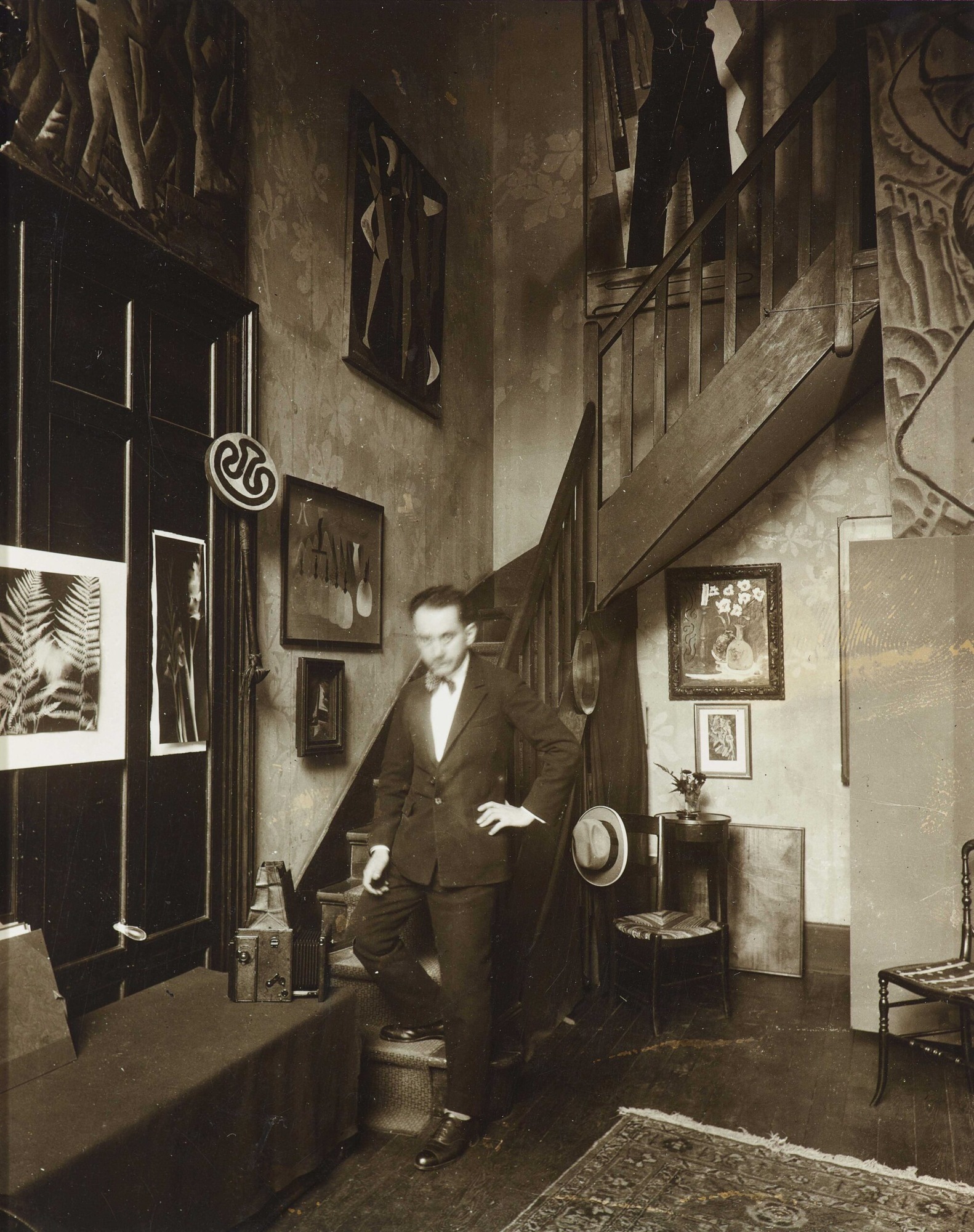 Man Ray debout dans son studio du 31 bis rue Campagne-Première en 1925, chambre photographique et rayographies accrochées au mur