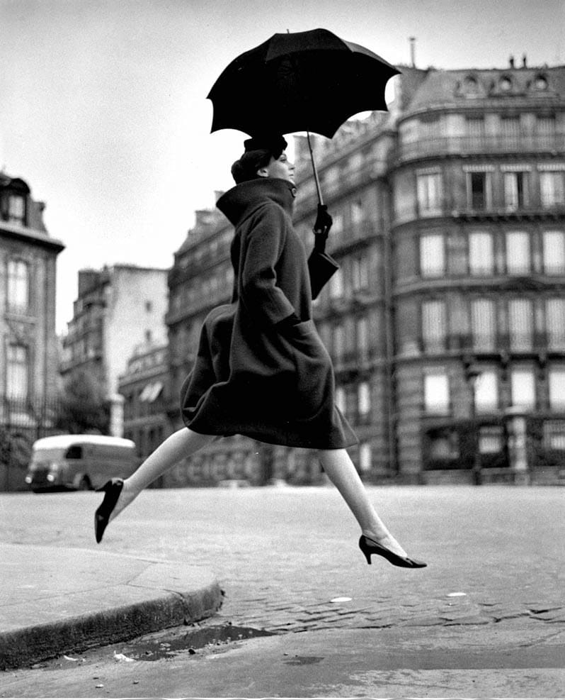 Carmen Dell'Orefice saute une flaque sous un parapluie, manteau Cardin, place François-Ier, Paris, 1957, par Richard Avedon
