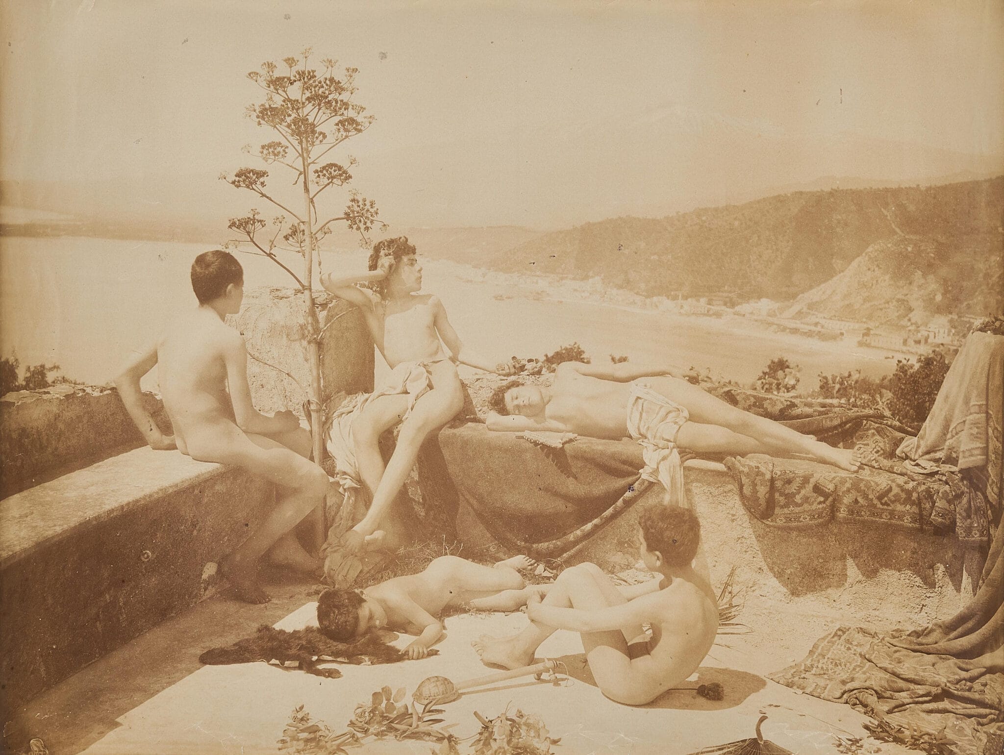 Wilhelm von Gloeden, Taormine, vers 1900. La baie en contrebas, l’agave, les draperies : tout le décor est là pour faire passer la scène.