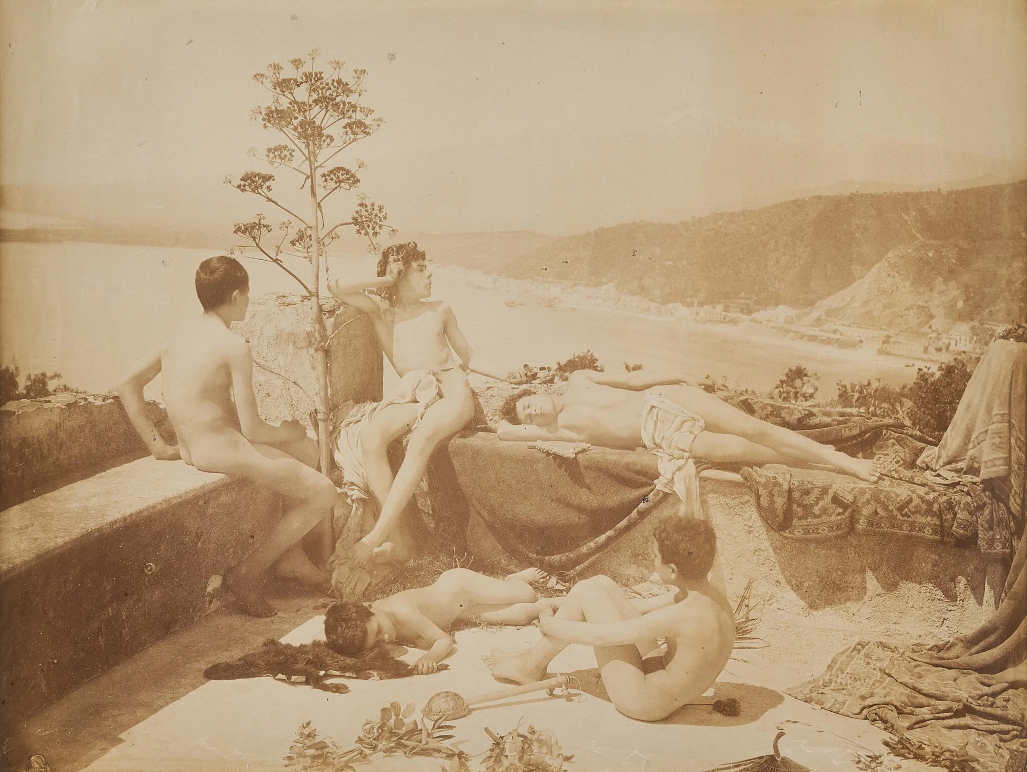 Wilhelm von Gloeden, Taormine, vers 1900. La baie en contrebas, l’agave, les draperies : tout le décor est là pour faire passer la scène.