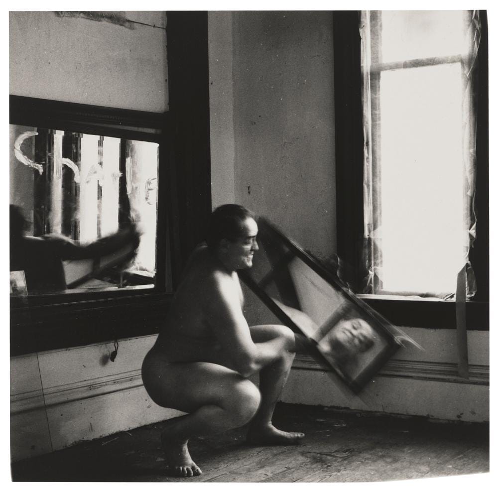 Charlie the Model #5, Providence, Rhode Island, 1976, Francesca Woodman : un modèle nu accroupi tenant un cadre devant une fenêtre