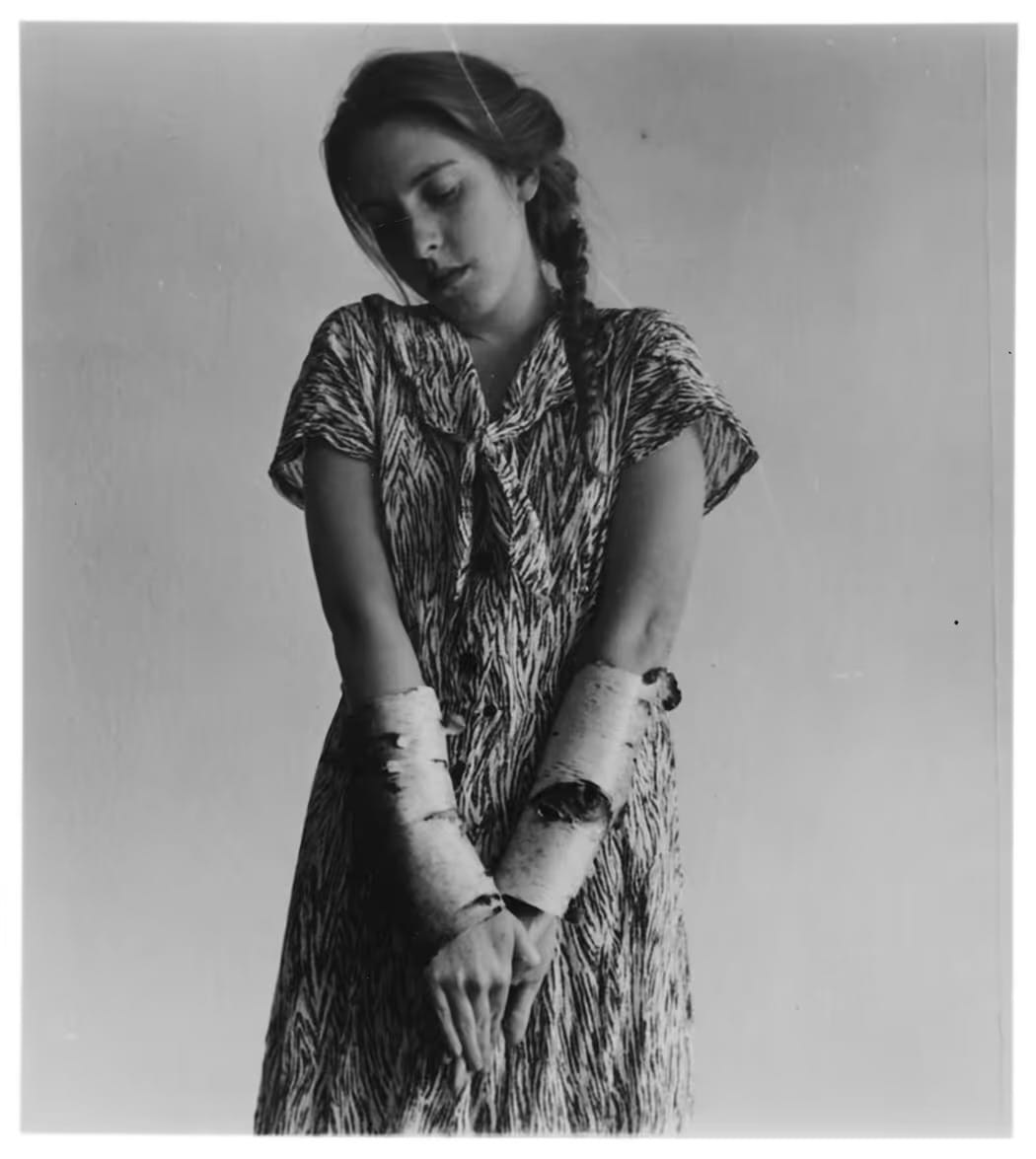 Francesca Woodman debout en robe imprimée, les avant-bras enveloppés de papier, New York 1980